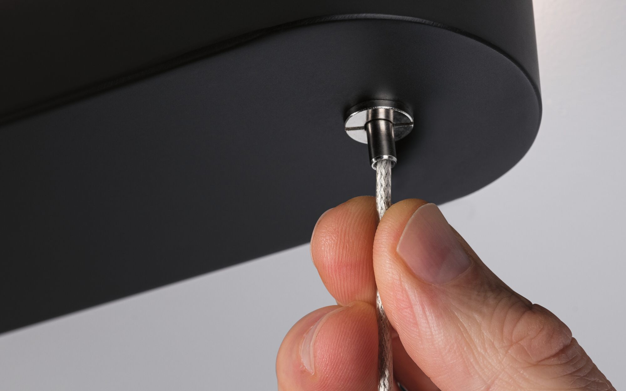 Hand houdt zilverkleurige stalen kabel vast aan zwart metalen onderdeel, close-up verlichtingsaccessoire