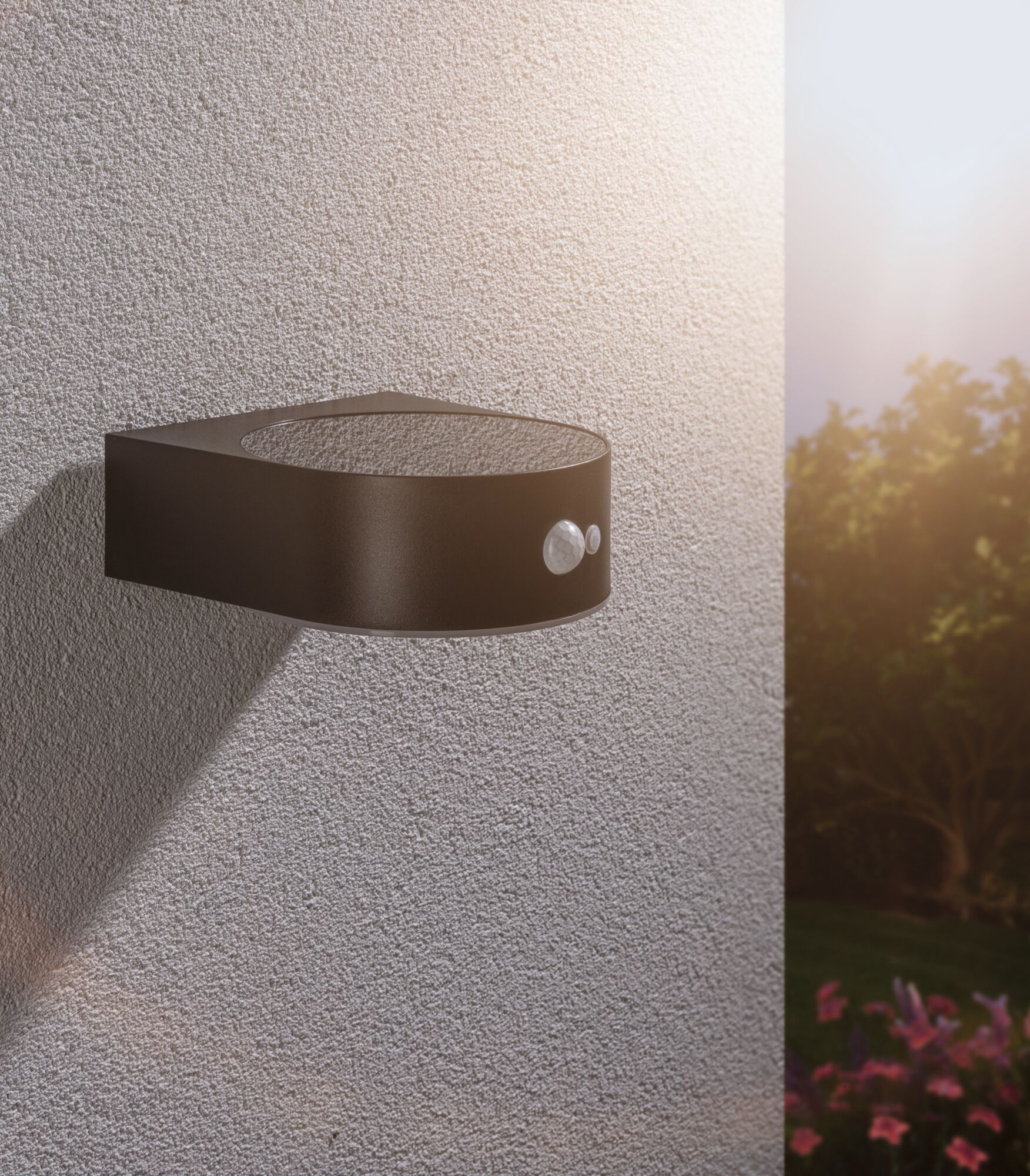 Zwarte metalen buitenwandlamp met bewegingssensor op gestructureerde muur bij zonsondergang