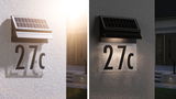 Solar-powered house number 27c with black casing and illuminated transparent sign on white wall