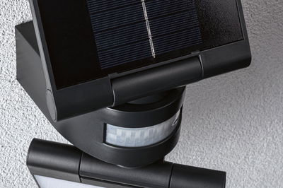 Schwarze Solarleuchte mit Bewegungsmelder und Kunststoffgehäuse an grauer Wand für Außenbeleuchtung