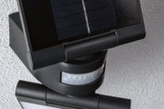 Schwarze Solarleuchte mit Bewegungsmelder und Kunststoffgehäuse an grauer Wand für Außenbeleuchtung