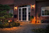 Illuminated house entrance with white doors, red brick walls, and warm outdoor lights along garden path.