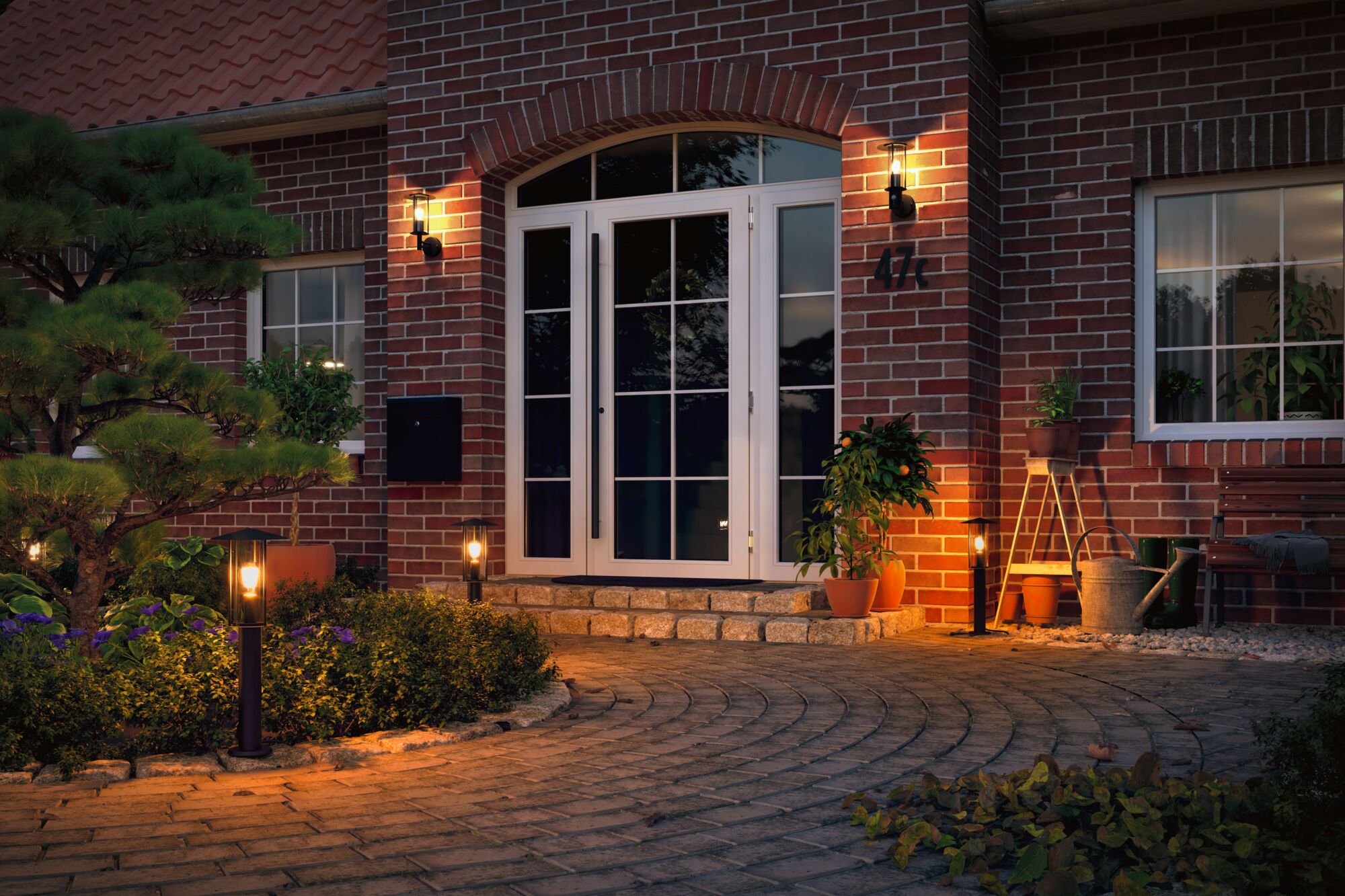 Illuminated house entrance with white doors, red brick walls, and warm outdoor lights along garden path.
