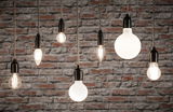 Various filament light bulbs with black sockets hanging in front of grey stone wall for decorative lighting