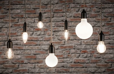 Various filament light bulbs with black sockets hanging in front of grey stone wall for decorative lighting