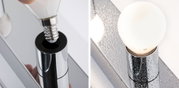 Nahaufnahme einer verchromten Lampenfassung mit E14 LED-Glühbirne und Wassertropfen auf Oberfläche