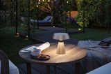 Beleuchtete tragbare Outdoor-Tischlampe in Beige auf Holztisch mit Tasse und Keks im Garten