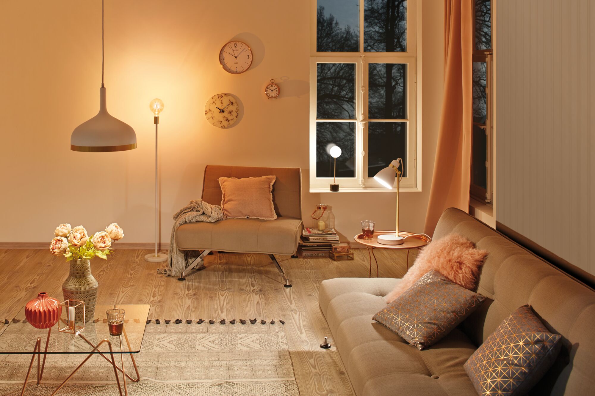 Gezellige woonkamer met beige meubels, warm wit licht, decoratieve kussens en wandklokken.