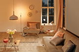 Gezellige woonkamer met beige meubels, warm wit licht, decoratieve kussens en wandklokken.