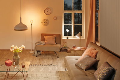 Gemütliches Wohnzimmer mit beigen Möbeln, warmweißer Beleuchtung und dekorativen Kissen und Uhren.
