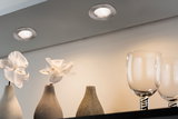 Two round brushed metal recessed lights illuminating white orchids in gray vases and glassware.