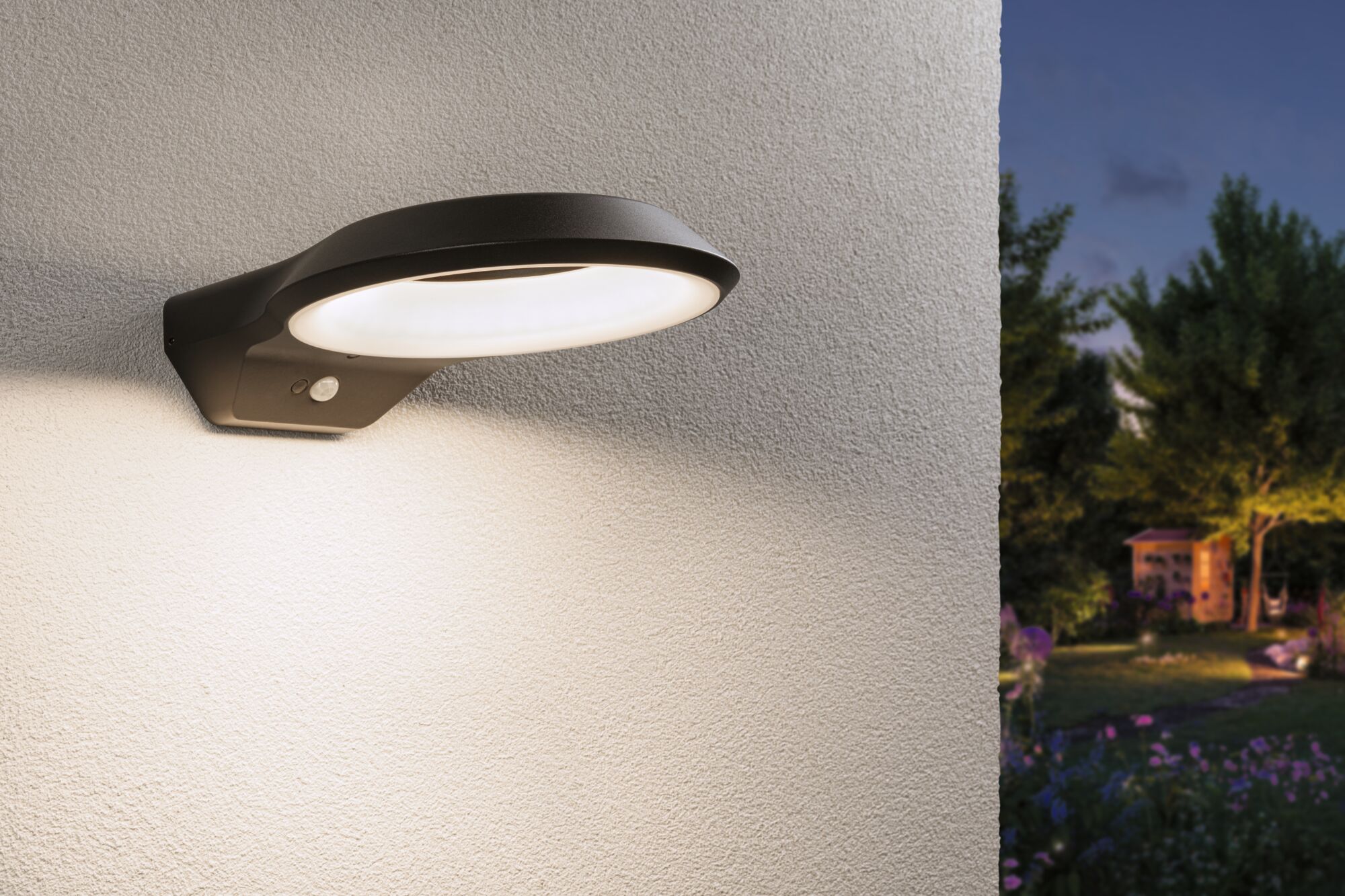 Moderne schwarze LED-Außenwandleuchte mit Bewegungsmelder an weißer Wand beleuchtet Gartenweg bei Dämmerung