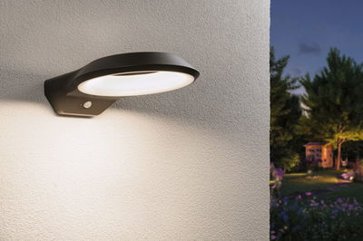 Moderne schwarze LED-Außenwandleuchte mit Bewegungsmelder an weißer Wand beleuchtet Gartenweg bei Dämmerung