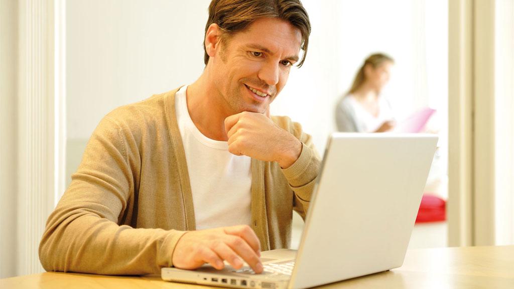 Mann in beigem Cardigan arbeitet konzentriert an Laptop in hellem Büro, Karriere und Arbeitsthema