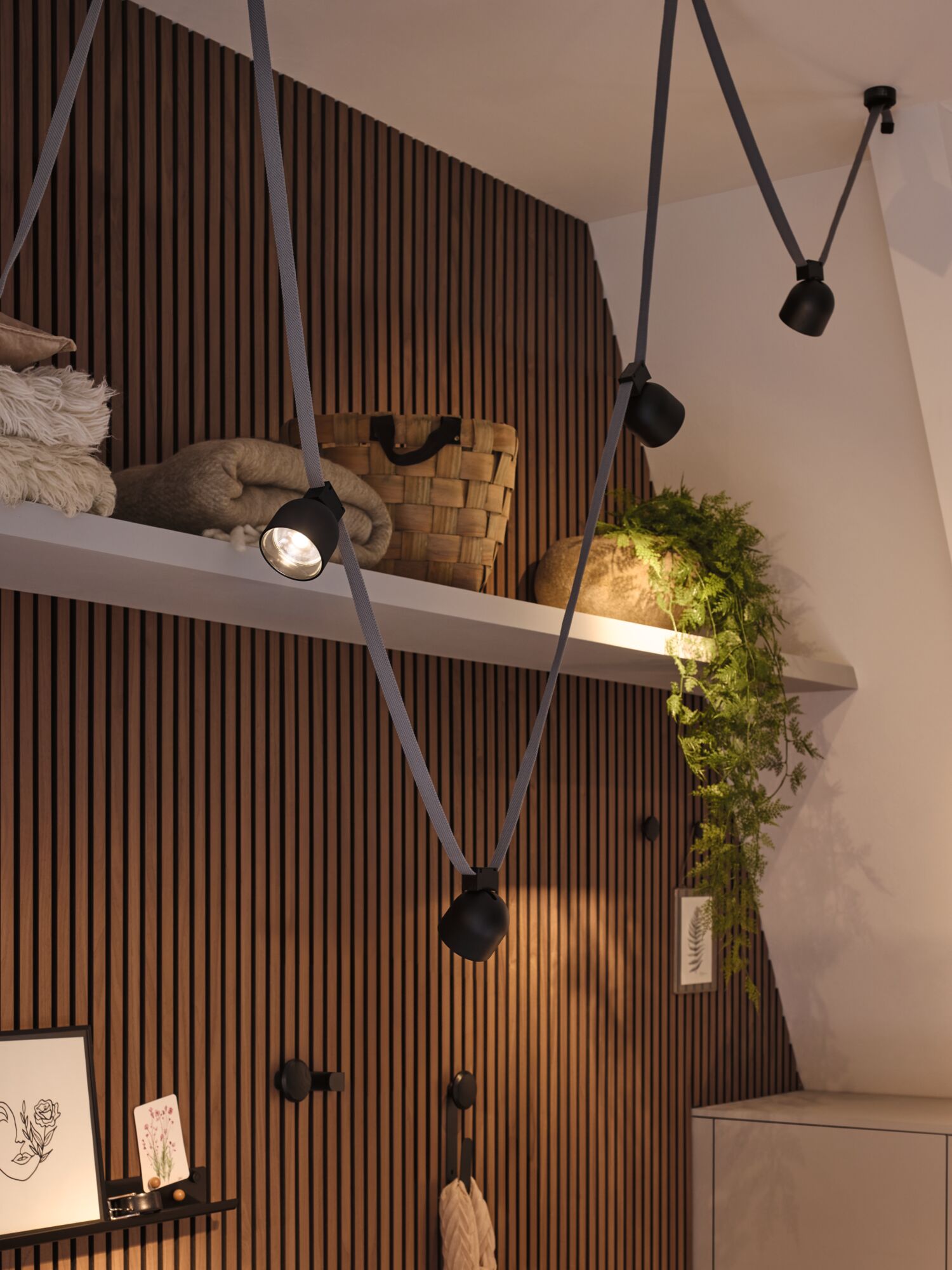 Modern black cable spotlights on grey cords against wooden slat wall with decor and plants.