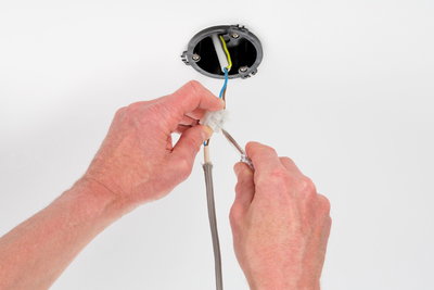 Hands connecting electrical wires with screw terminal on white ceiling for lighting installation
