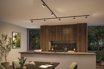 Moderne keuken met houten kasten en zwart aanrecht, verlicht door zwarte LED-plafondspots.