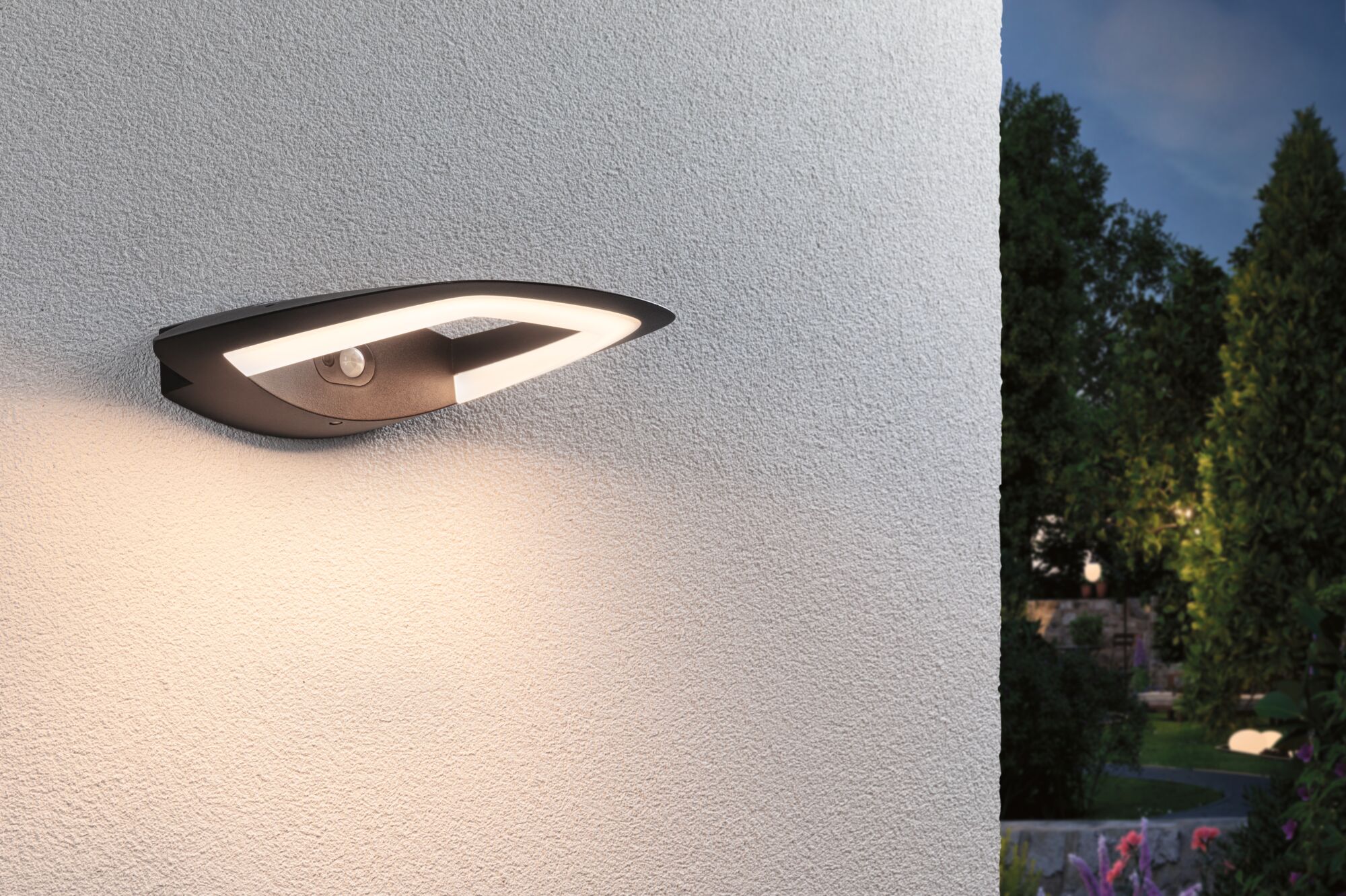 Moderne zwarte LED-buitenwandlamp met bewegingssensor gemonteerd op witte muur in tuin