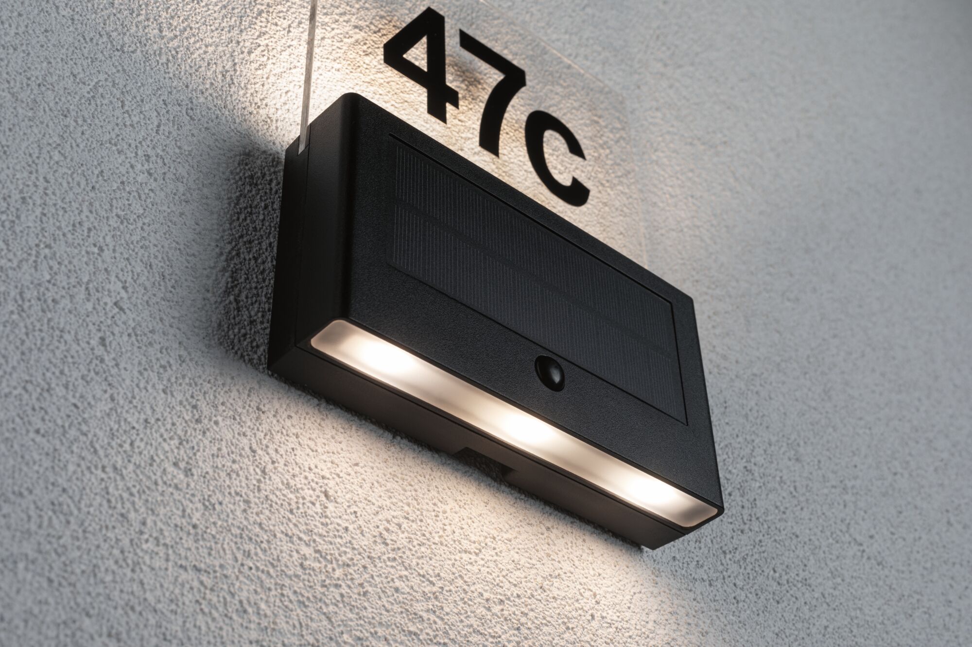 Black solar LED house number light with motion sensor and illuminated number 47c on white wall