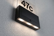 Schwarze Solar-LED-Hausnummernleuchte mit Bewegungsmelder und beleuchteter Nummer 47c an weißer Wand