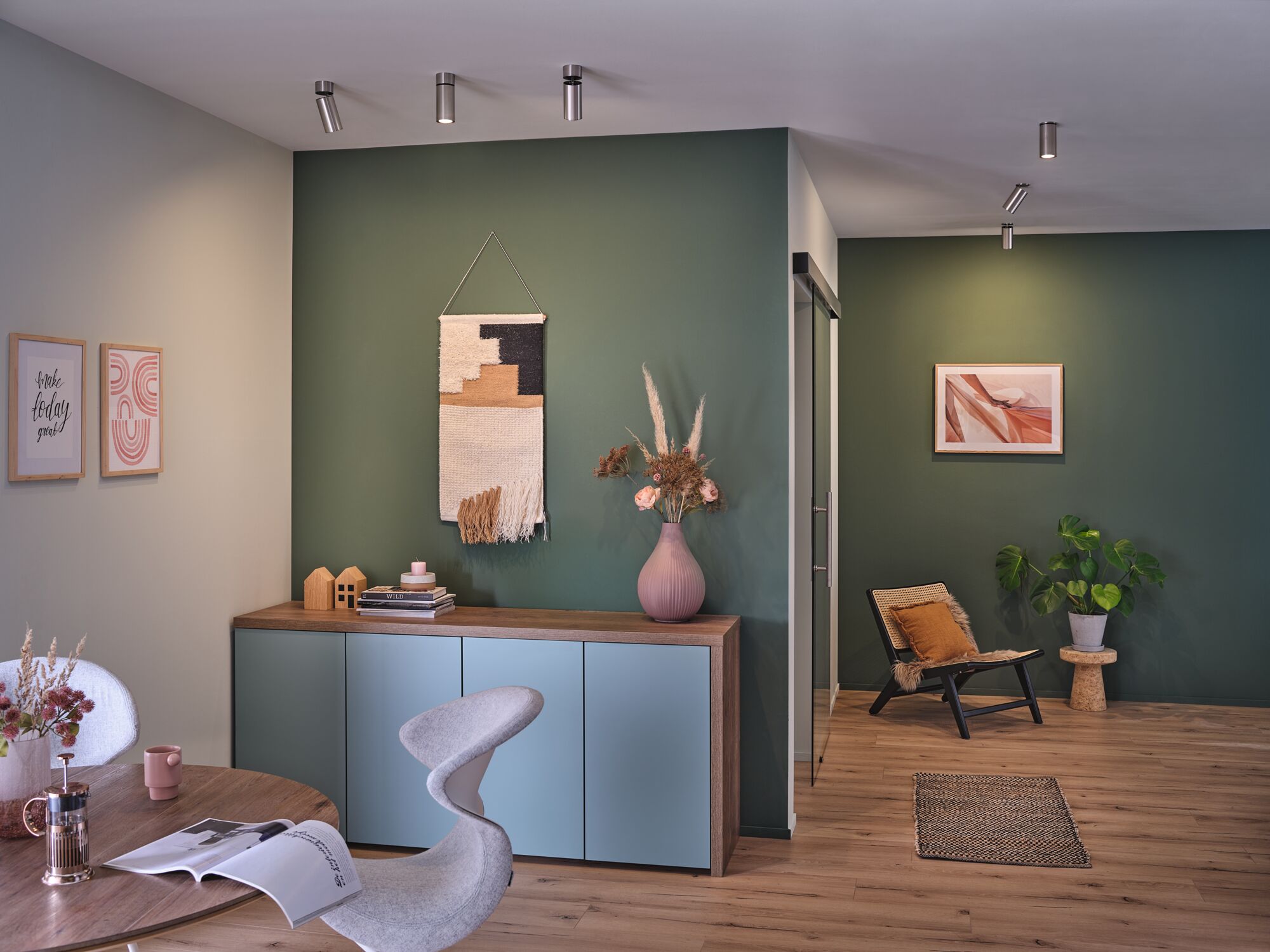 Salon moderne avec mur vert, buffet en bois, vase décoratif et spots de plafond en métal élégants.