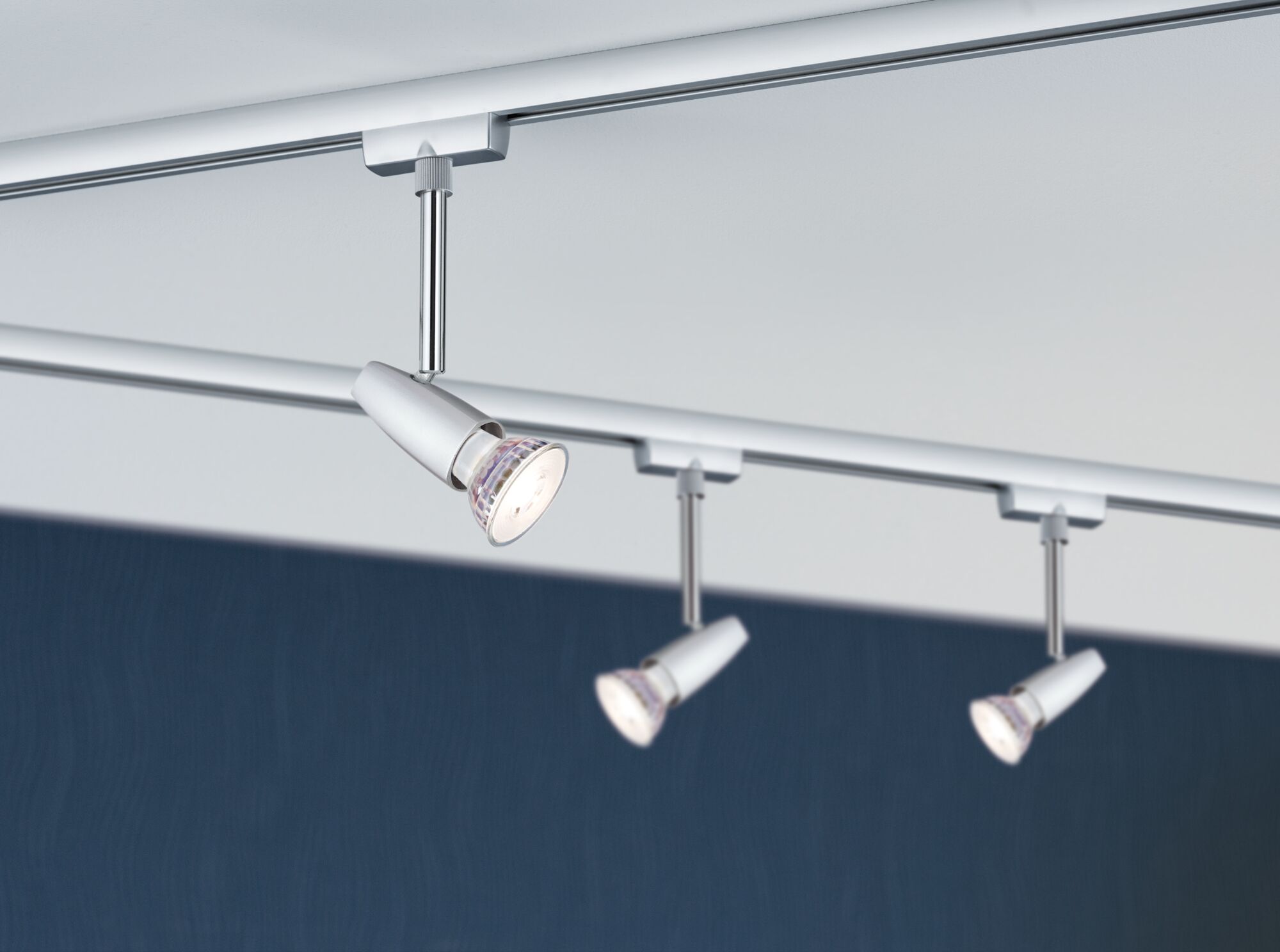 Drie witte metalen LED-spotlights aan een plafondrail voor verstelbare verlichting