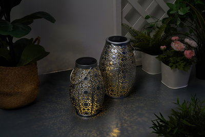 Two silver solar metal lanterns with intricate patterns and warm light for atmospheric garden decoration.