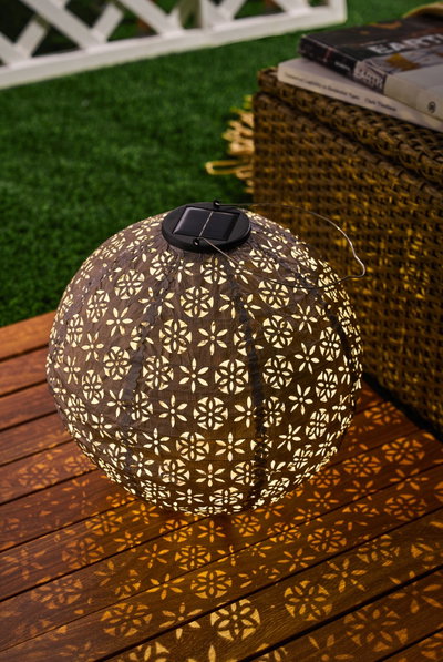 Solar-powered brown metal garden lantern with decorative pattern casting warm light for outdoor use