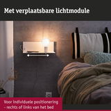 Wit wandplankje met verplaatsbare lichtmodule en warm LED-licht naast bed met gebreide deken