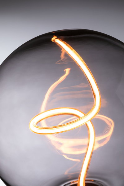 Close-up of warm white LED filament bulb with curved glowing filament inside clear glass.