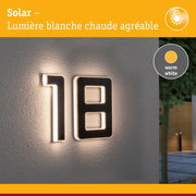 Numéro de maison solaire en matériau noir avec lumière LED blanc chaud sur mur gris