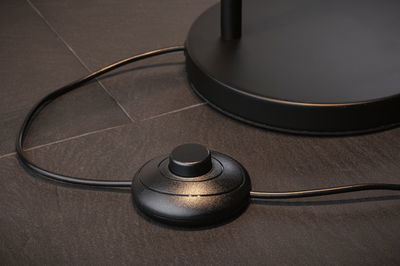 Zwarte ronde kunststof voetschakelaar op donkere vloer voor lampbediening met kabel.