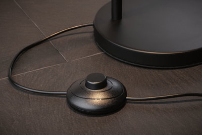 Interrupteur au pied rond noir en plastique sur sol foncé pour commande de lampe avec câble.