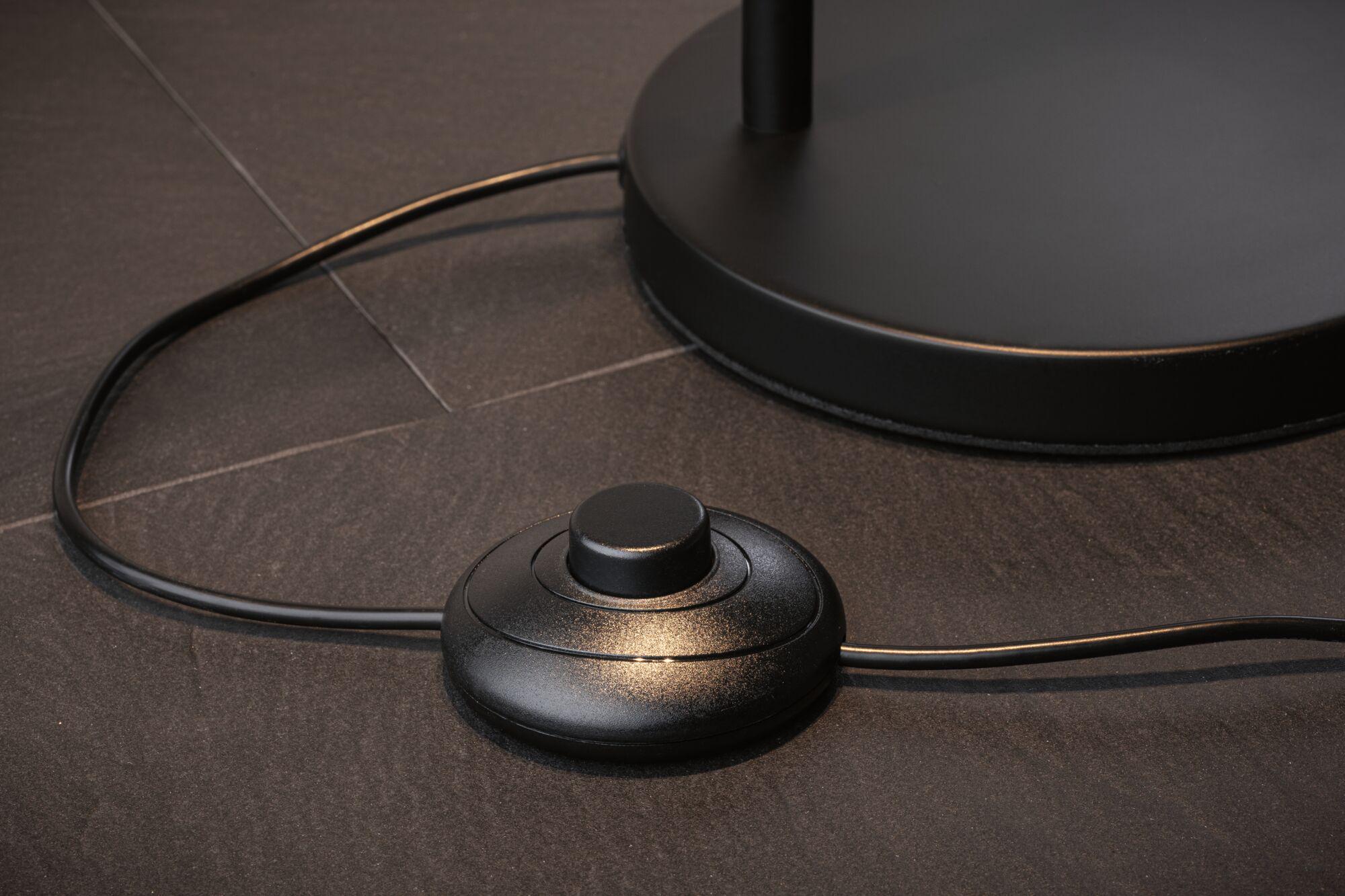Black round metal foot switch on dark floor with cable for lamp control and lighting