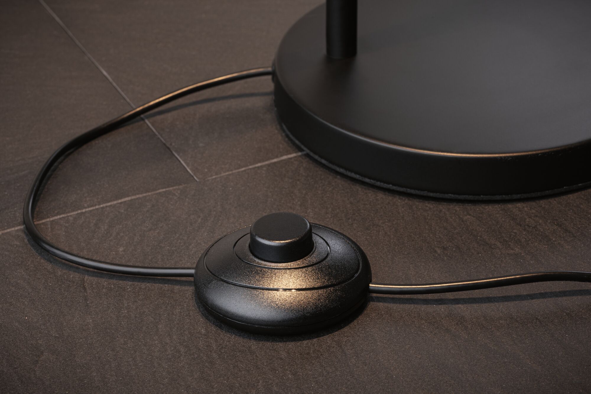 Black round metal foot switch on dark floor with cable for lamp control and lighting