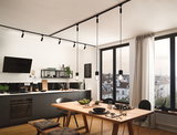 Cuisine moderne avec meubles noirs, table en bois et suspensions noires sur rail d'éclairage.