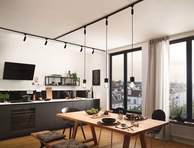 Modern kitchen with black cabinets, wooden dining table, and black pendant lights on track lighting system.