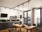 Modern kitchen with black cabinets, wooden dining table, and black pendant lights on track lighting system.