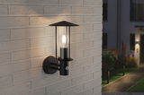 Black metal outdoor wall light with clear glass and motion sensor on light brick wall