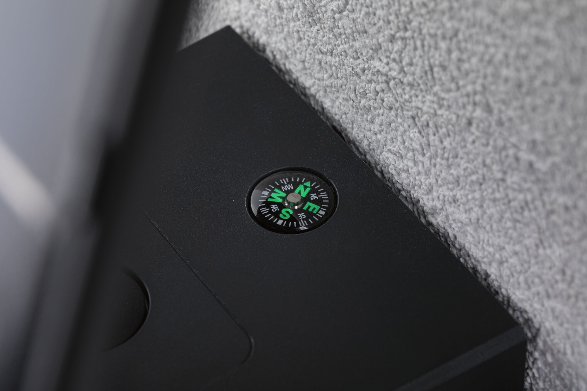 Black casing with built-in compass showing green directions on a grey textured surface