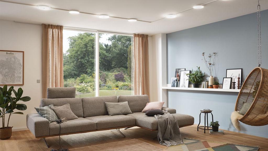 Modernes Wohnzimmer mit grauem Stoffsofa, Rattanhängesessel und indirekter Deckenbeleuchtung für gemütliche Atmosphäre.