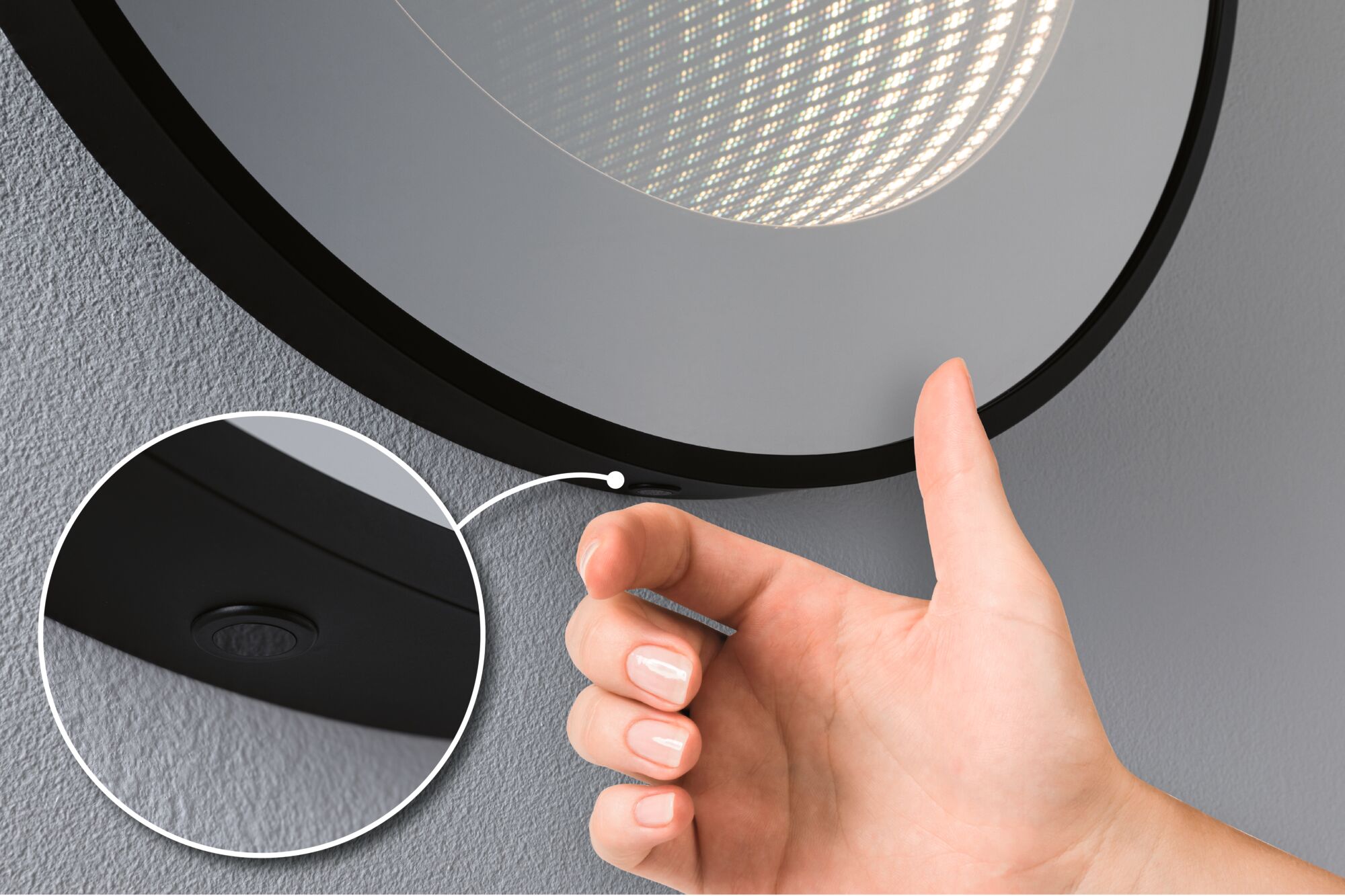 Main actionnant une lampe miroir LED noire avec interrupteur intégré sur mur gris pour éclairage salle de bain