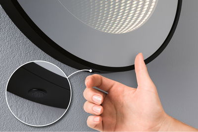 Hand operating black LED mirror light with built-in switch on grey wall for bathroom lighting