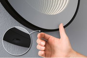 Main actionnant une lampe miroir LED noire avec interrupteur intégré sur mur gris pour éclairage salle de bain