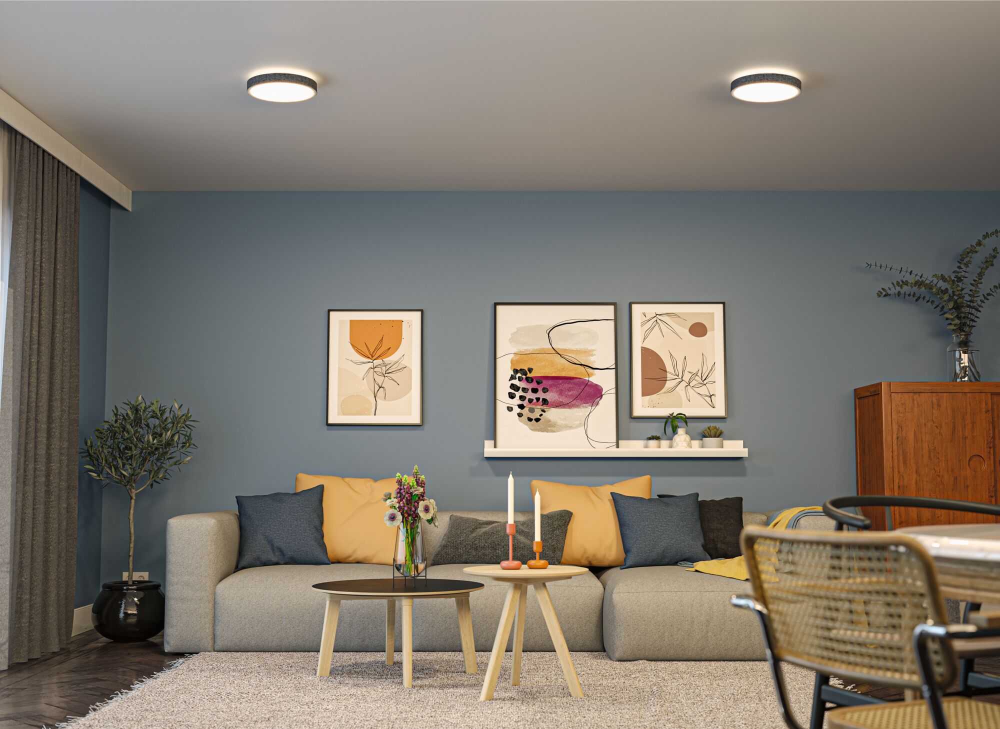 Modernes Wohnzimmer mit zwei runden Deckenleuchten in Weiß und Holz-Couchtischen vor grauem Sofa mit bunten Kissen.