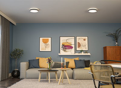 Modernes Wohnzimmer mit zwei runden Deckenleuchten in Weiß und Holz-Couchtischen vor grauem Sofa mit bunten Kissen.