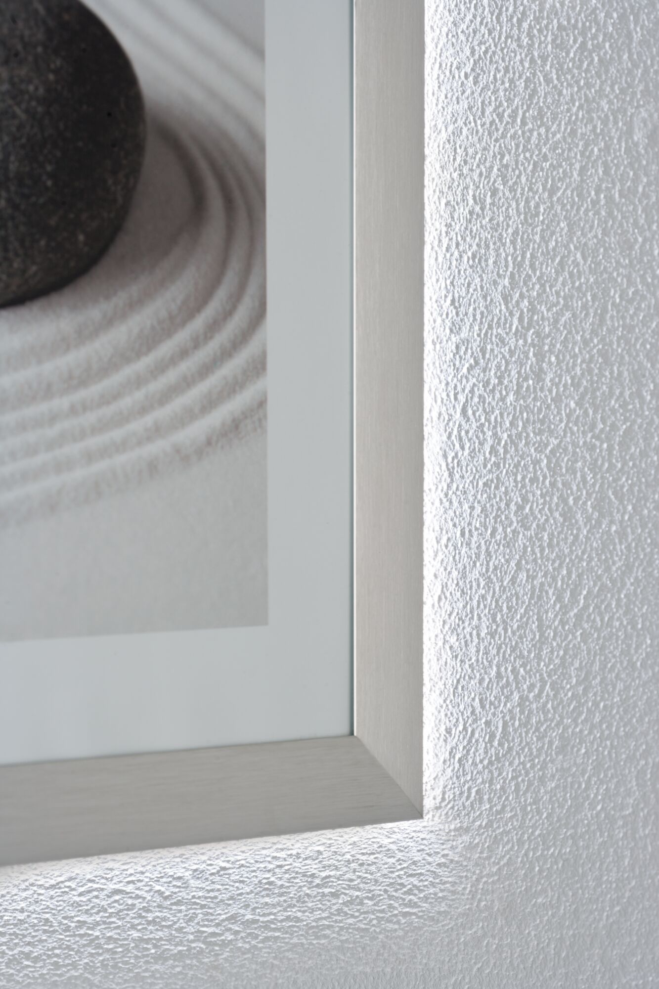 Close-up of silver aluminum frame with indirect LED wall lighting and textured white wall surface.