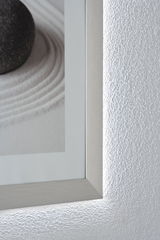 Close-up of silver aluminum frame with indirect LED wall lighting and textured white wall surface.