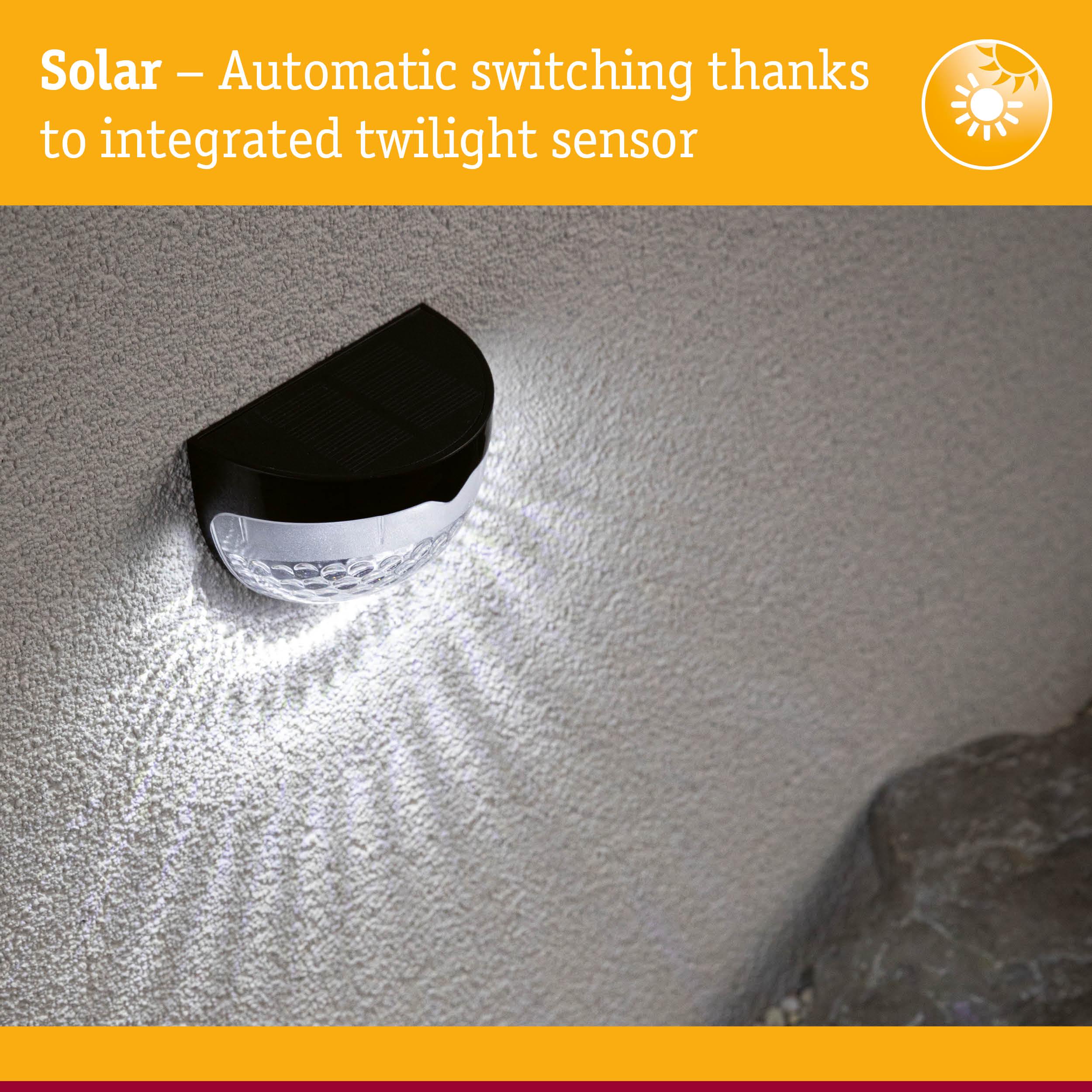 Black solar wall light with integrated twilight sensor casting white light on textured wall