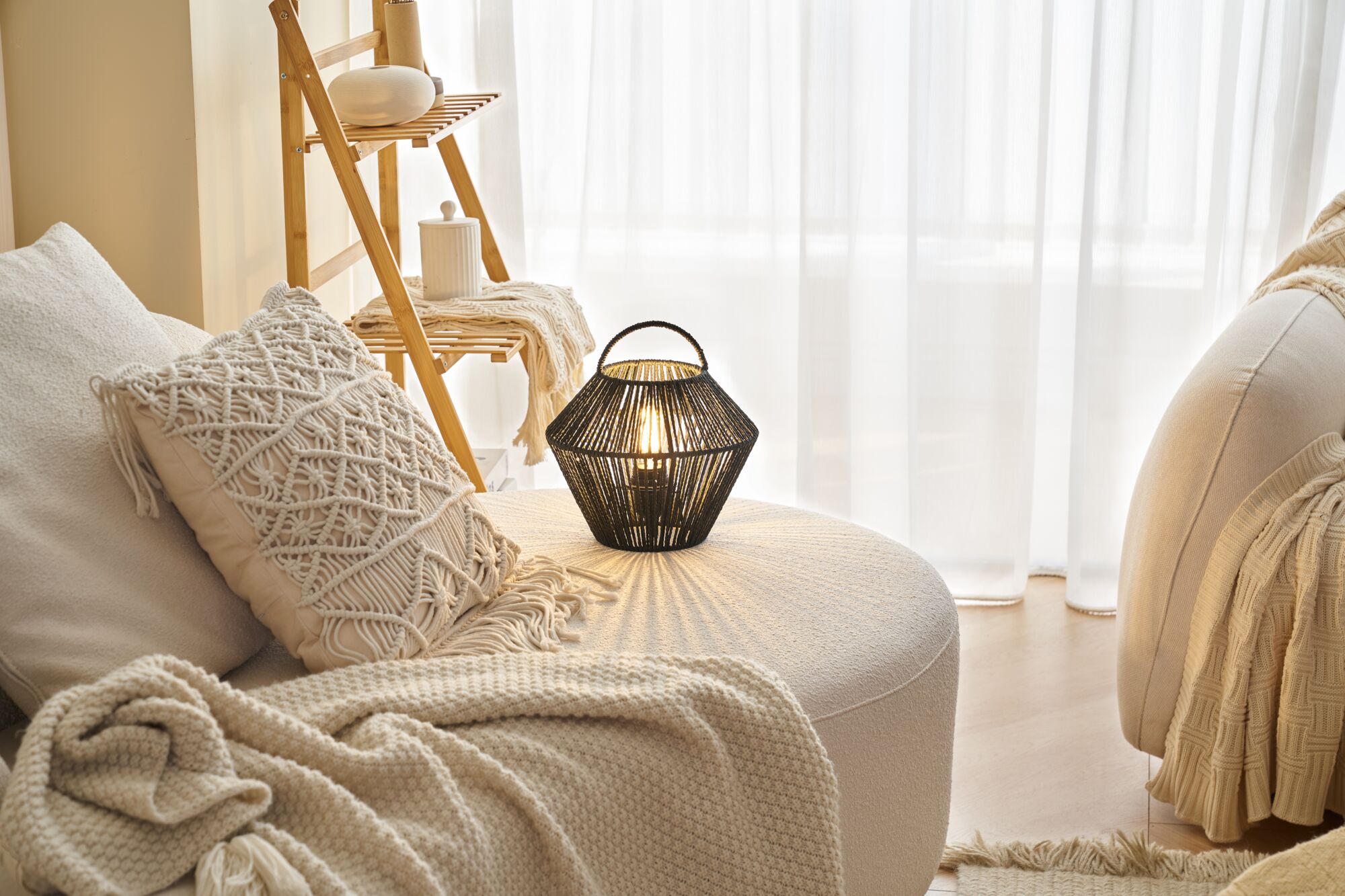 Schwarze Laterne aus geflochtenem Material auf cremefarbenem Sofa mit Kissen und Decke im Wohnzimmer